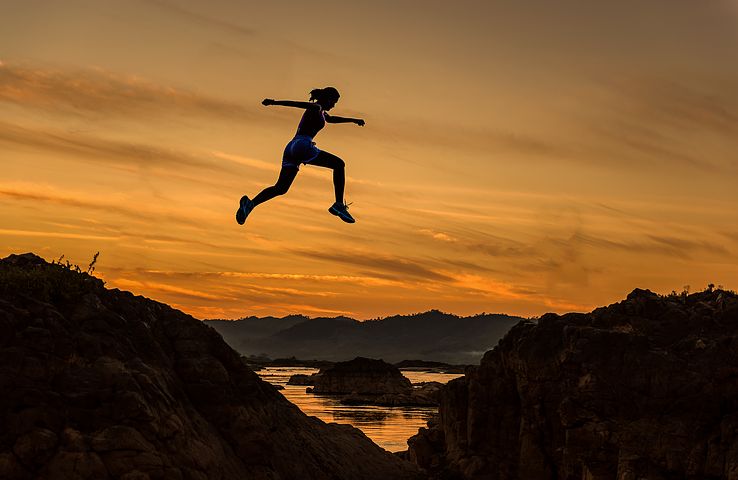 Woman leaping over cravass at sunset